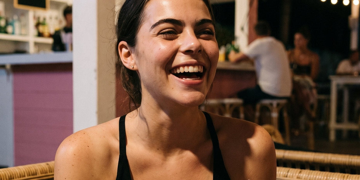 Woman in a black plunge top laughing at a beach bar