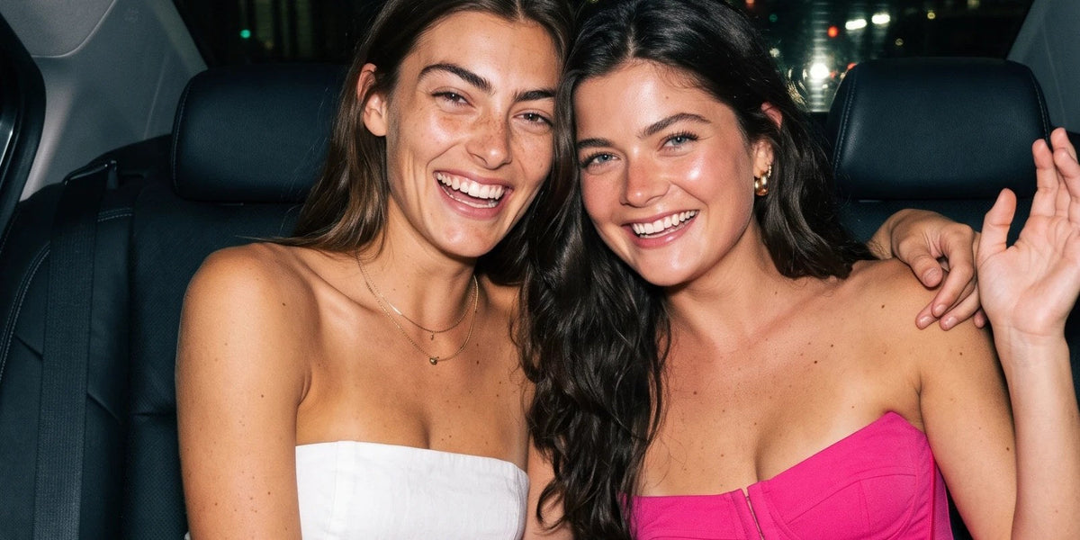 Two friends in strapless dresses laughing in the back of a car