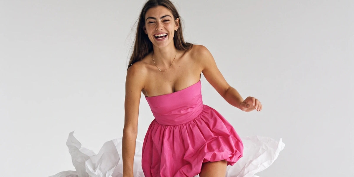 Woman in a pink strapless bubble dress sitting on a giant Sticky Boobs box