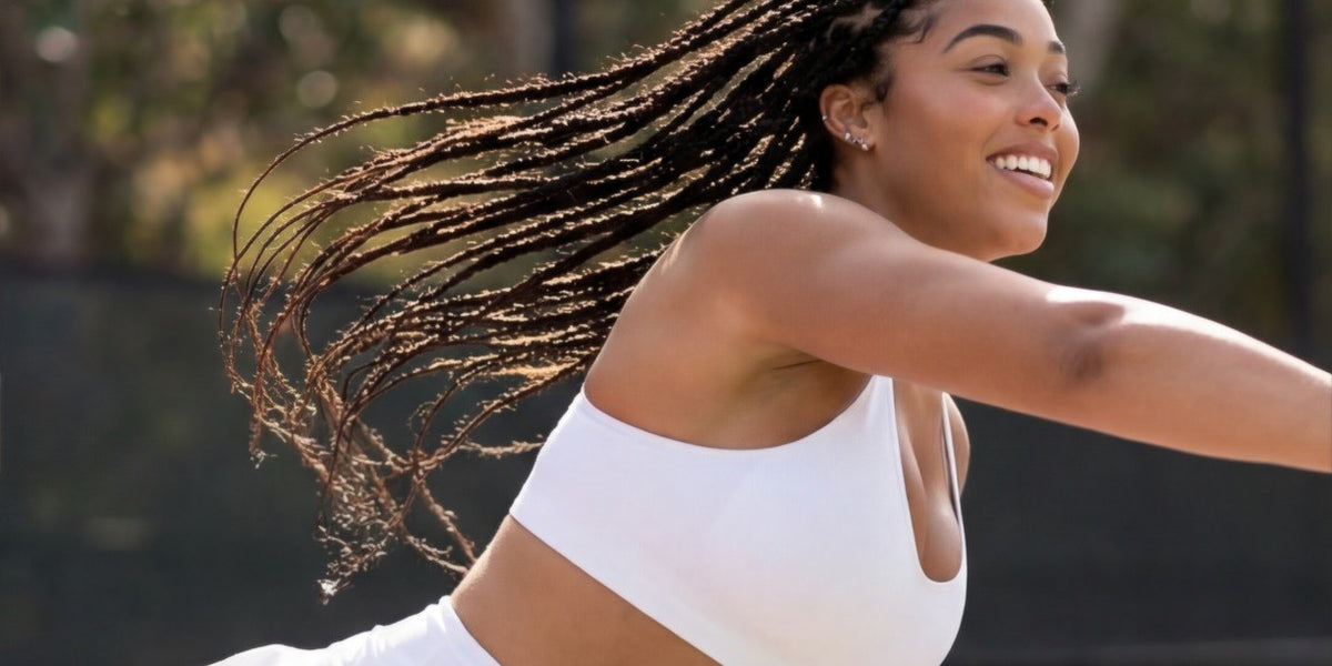 Woman in a white sports top and tennis skirt mid-swing