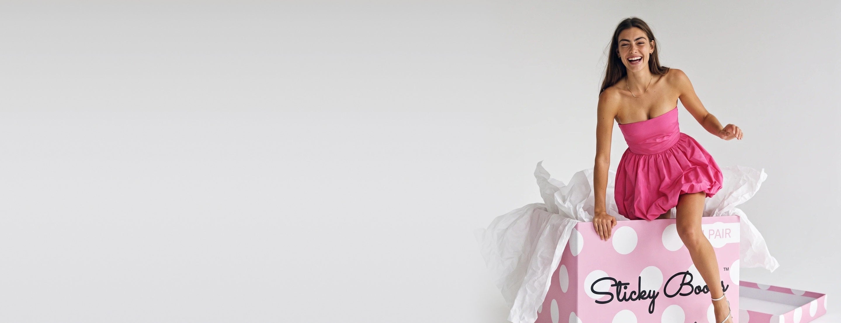 Laughing as she climbs out of a giant Sticky Boobs box in a pink strapless dress